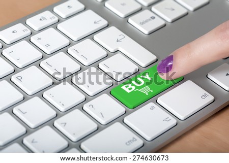 Internet shopping. Female finger clicking on BUY button on computer keyboard with white buttons but green shopping button with cart symbol