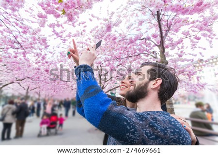 Hipster couple taking photos of cherry blossoms in Stockholm with smart phone at Kungstradgarden, the swedish for Garden of King. Love and friendship concepts with a hipster theme.