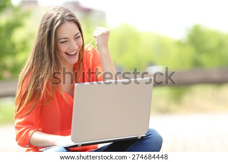 Euphoric woman searching job with a laptop in an urban park in summer Royalty-Free Stock Photo #274684448