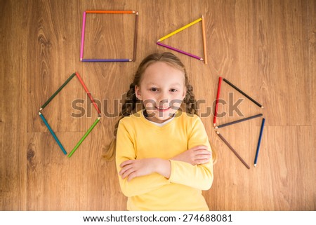 Little pretty smiling girl in yellow  pullover  laying on the floor with color pencils.