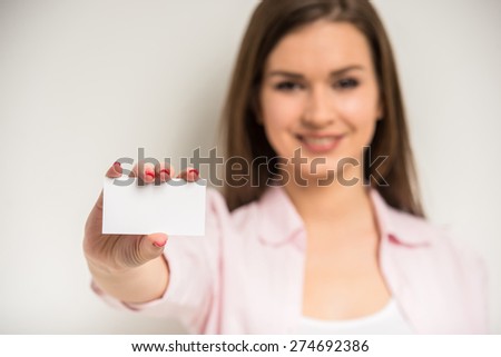 Young smiling beautiful girl with business card showing empty open space for text on grey background.