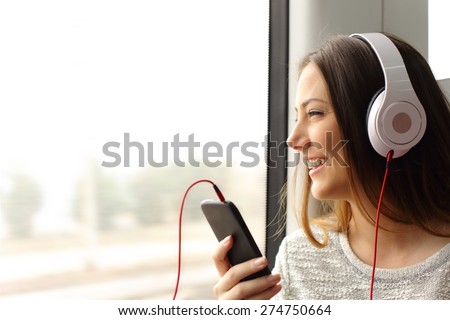 Happy teen passenger listening to the music traveling in a train and looking through the window Royalty-Free Stock Photo #274750664