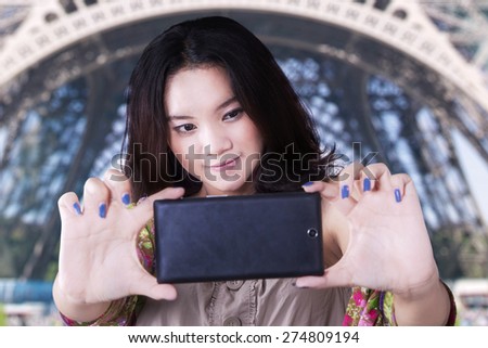 Beautiful asian teenage girl using smartphone to take a selfie near the Eiffel Tower in Paris