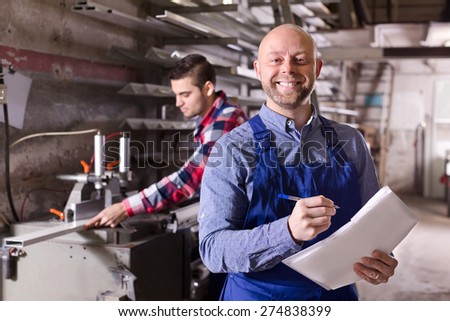 Positive  worker operating in lathe, his boss with papers nearby