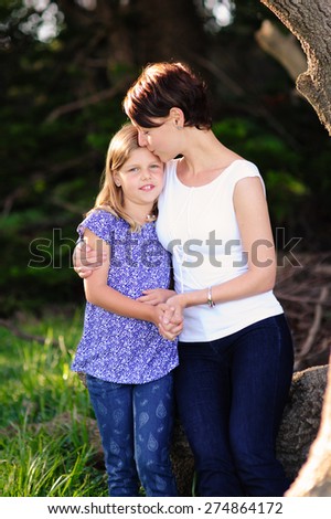 A close up portrait of a young beautiful mum and her adorable daughter outdoors in a park on a sunny summer day