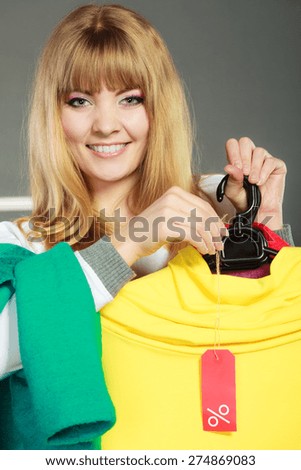 Good shopping sale concept. Blonde fashionable woman choosing clothes holding discount red label with percent sign in hand