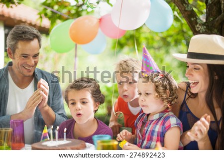 garden party with family for little girl's birthday, children blows out the candles on the cake, the garden is decorated with balloons and colors are bright