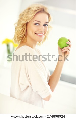 A picture of a young woman eating apple in the kitchen
