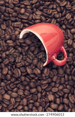 Closeup of dark roasted coffee beans spilling from a red cup. Food and drink backdrop showing aromatic and beautiful coffee beans. 