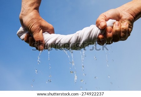Hands squeeze wet fabric against blue sky. Royalty-Free Stock Photo #274922237