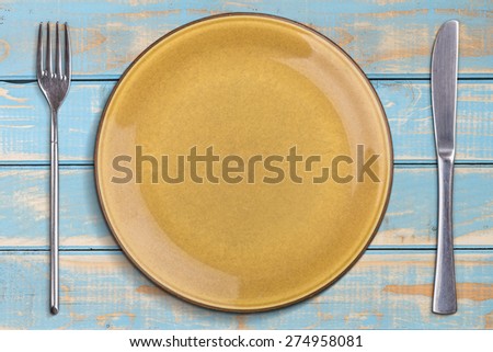 Empty plate with knife and fork on blue wooden table
