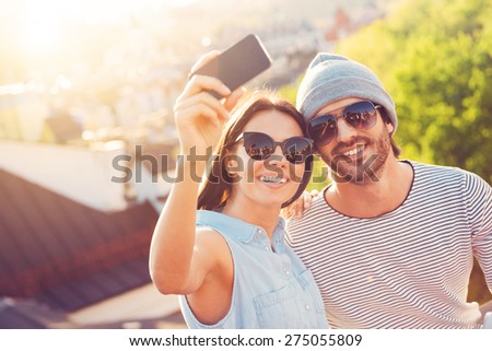 Capturing the brightest moments. Beautiful young couple making selfie by smart phone and smiling while sitting together on the roof of the building  