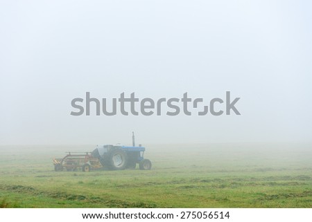 Blue tractor sitting in an empty foggy field in the morning, Stowe, Vermont, USA.