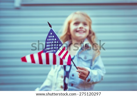 Flying american flag in little girl's hand. Selective focus, blurred background. Independence Day, Flag Day concept. Vintage and retro toning. Instagram filters