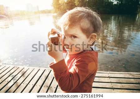 Portrait of a smiling cute boy taking picture with retro camera at a lake