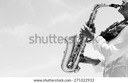 Saxophonist playing on saxophone on blue sky background  Royalty-Free Stock Photo #275322932