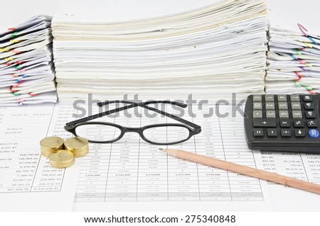 Brown pencil with black spectacles and gold coins have pile of paperwork as background. Stack of paperwork is high as work hard. Business and finance concepts rich and successful photography.