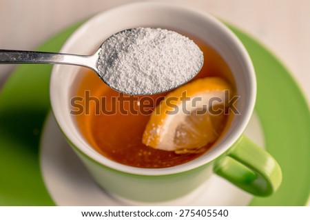 Sweetener is poured from a spoon in a cup of tea