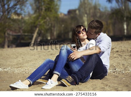 Cheerful couple embracing and posing on the beach on a sunny day. Picture (photo) of a happy couple having fun on the beach, listen music by phone. Hipster style. Outdoor shot