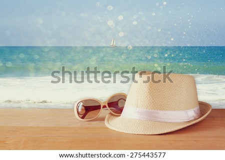 fedora hat and sunglasses over wooden table and sea landscape background. relaxation or vacation concept

