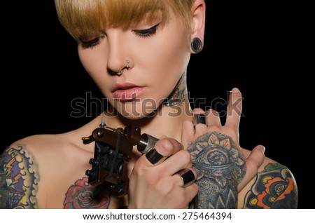 tattooed young woman with tattoo machine, dark background