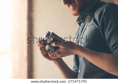 Hipster young man holding a vintage camera and checking settings