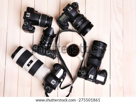 Modern cameras and cup of coffee on wooden table, top view