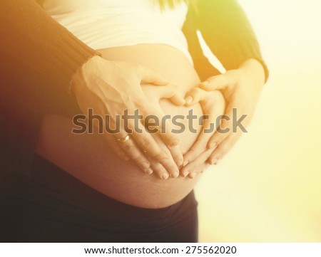 Pregnant couple with hands around belly making a heart shape