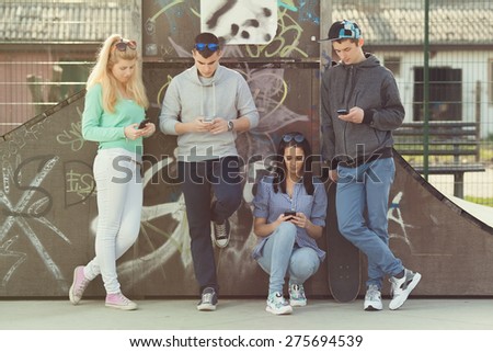 Group of young friends hanging out in a skate park and using mobile phones