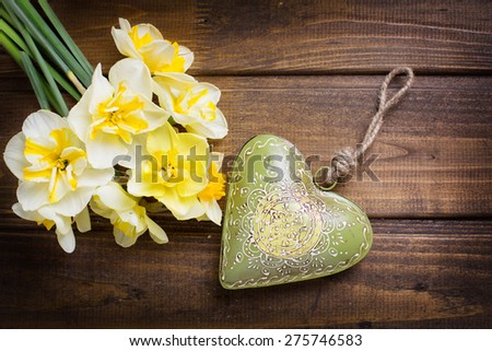 Fresh  spring yellow  daffodils  flowers and decorative heart  on brown painted wooden planks. Selective focus. Place for text. Toned image. 