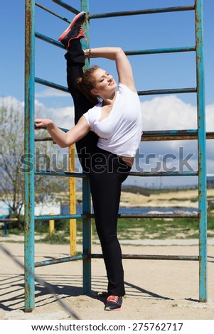 Girl athlete doing stretching exercise outside near horizontal bar, spring time
