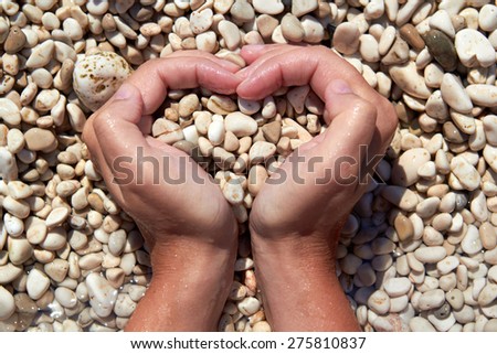 Hands in the form of heart with pebbles inside beach sunny day