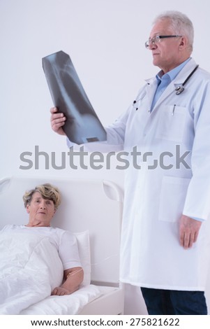 Doctor analyzing chest x-ray while patient lying in bed