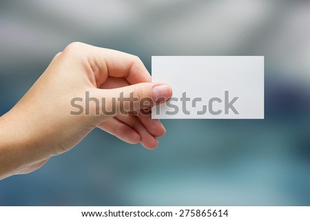 Hand holding white blank business card on blue blurred background. Copy space
