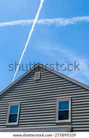 Suburban home with X crisscross plane clouds above.  Simple house with dynamic clouds above.