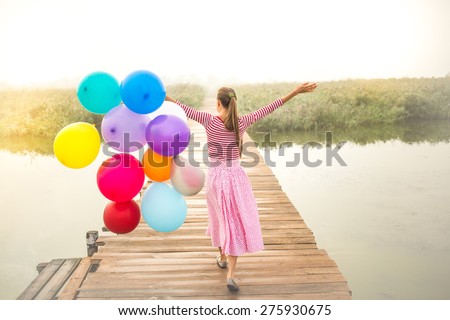 Vintage image of beautiful woman with colorful balloons walking on wooden bridge. grain added, in motion