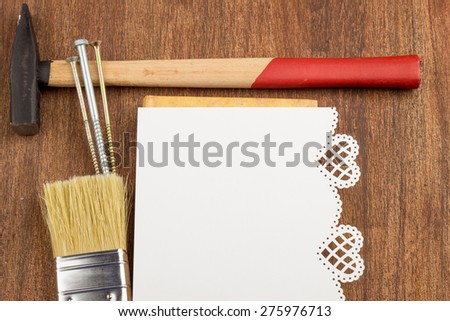 white sheet of paper with punching hearts, with punching flowers on a brown background, hammer, nails, screws, brush