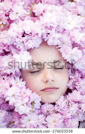 Face of small girl with closed eyes among pink flowers of japanese cherry blossom copyspase, horizontal picture