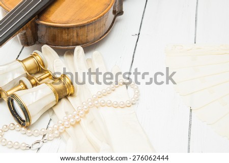 Vintage backgrop with violin, white leather gloves, fan, pearl beads and binoculars on a white wooden background 