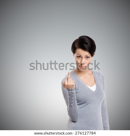 Attractive woman shows a vulgar, obscene finger sign, isolated on grey