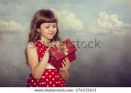 Little girl in vintage spotted red dress holding her present. Closeup. Photo in retro style with old textured paper.