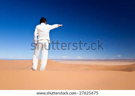 Rear view of an adult caucasian man standing on a sand dune pointing to somewhere. Erg Chebbi, Maroc
