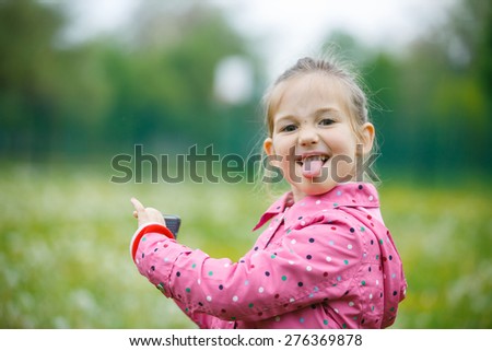 Little girl making faces and showing her tongue to her father that disturbed her at taking a picture with smart phone. Disobedience, cheerful behavior and carefree childhood concept. 