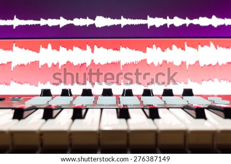 music keyboard synthesizer & waveform on screen monitor, shallow dept of field & focus on knobs for digital recording studio concept
