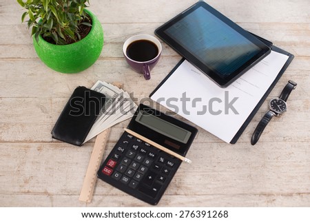 Creative top view photo of paper, watches, purse with money, pencil, calculator, straight edge tool, green plant, cup of coffee and tablet computer on the light-colored woodblocks