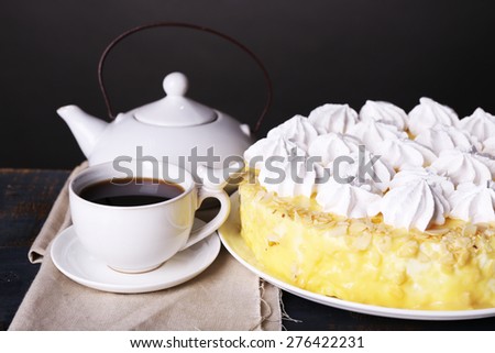 Tasty homemade meringue cake and cup of tea on wooden table, on grey background