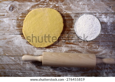 Ingredients for making pastry with flour and rolled dough on wooden table top in flour, horizontal picture