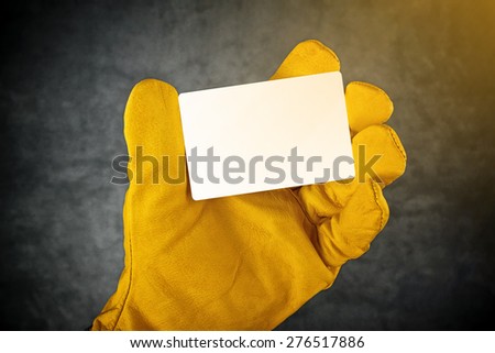 Male Hand in Yellow Leather Construction Working Protective Gloves Holding Horizontal Blank Business Card with Rounded Corners.