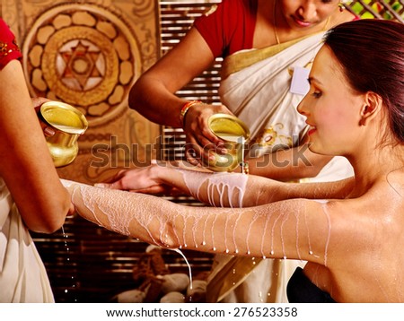 Woman having Ayurvedic spa treatment. Pouring milk. Picture on background.