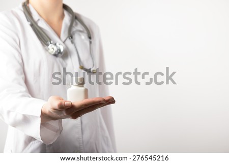 Female doctor holding up a bottle of tablets or pills with a blank white label for treatment of an illness or injury with focus to the bottle .Close up shot on grey blurred background. Copy space